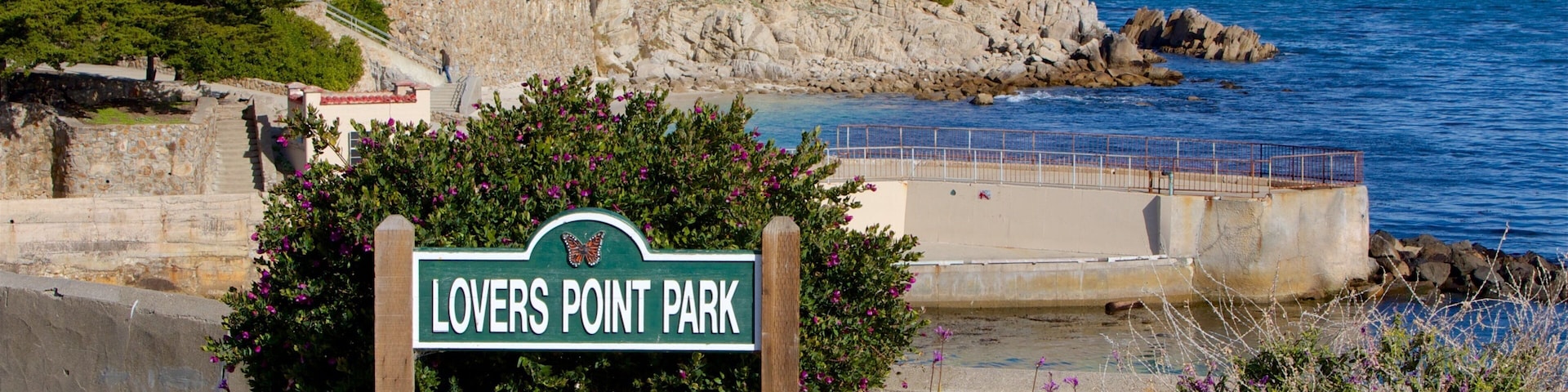 A sign for Lovers Point Park with a view of the ocean and rocky coastline.