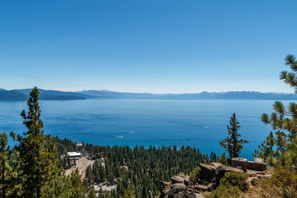 A mountainous landscape with a clear blue lake, dense forest, and a small building.
