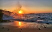 Un atardecer sobre una costa rocosa con olas rompiendo en la orilla.