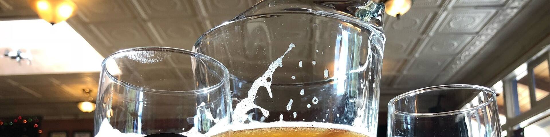 Tres vasos de cerveza, uno alto y dos bajos, con un logotipo de calavera, sobre una mesa de madera.