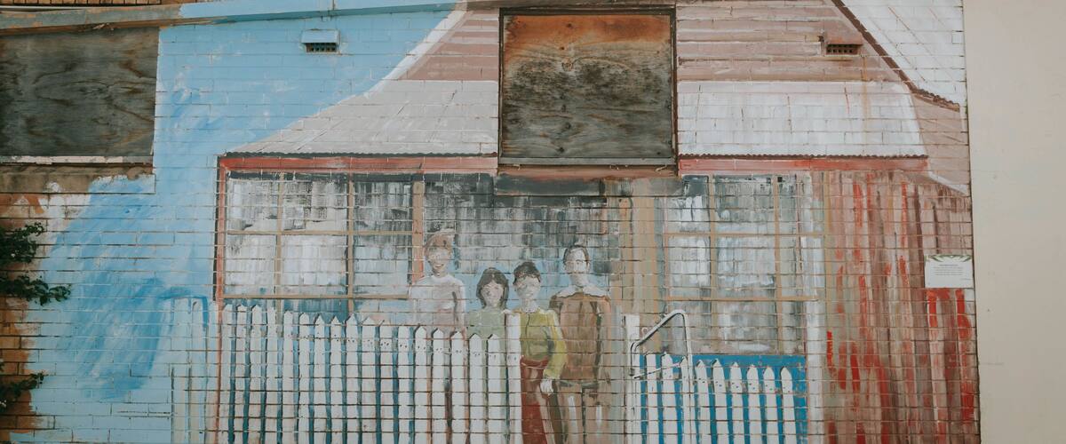 A mural of a building with a blue and white color scheme, a white picket fence, and a small window.