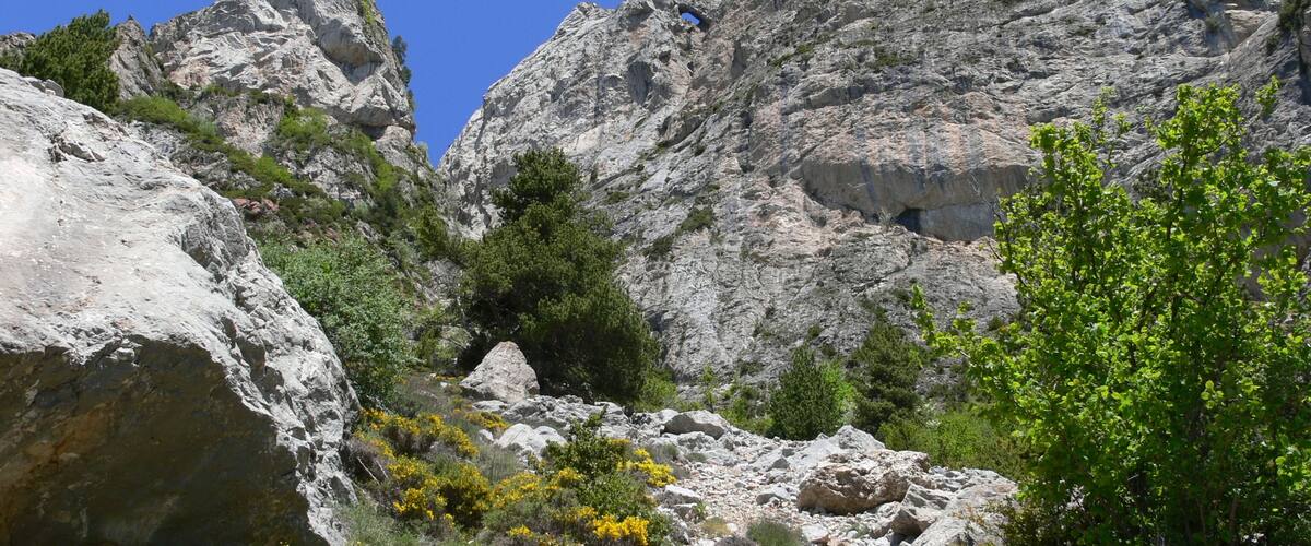 A rocky mountain landscape with sparse vegetation and a clear blue sky.