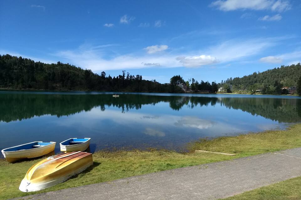 A calm lake with boats on the shore, surrounded by forested hills.