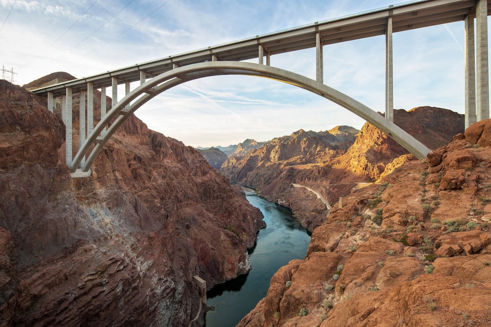 A large arched bridge over a river in a canyon with rocky terrain.