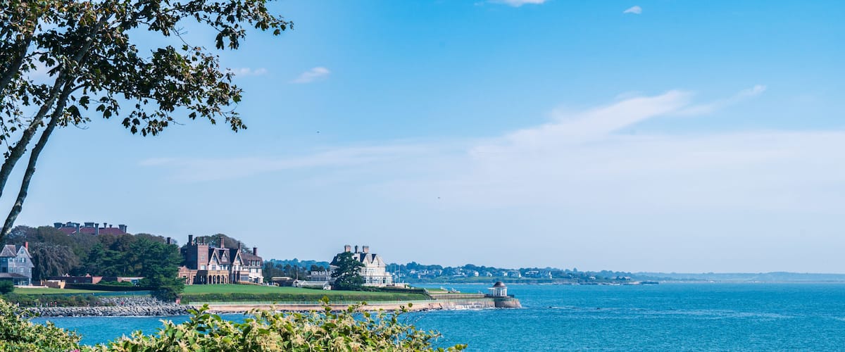 A coastal town with historic buildings, a lighthouse, and a clear blue sky.