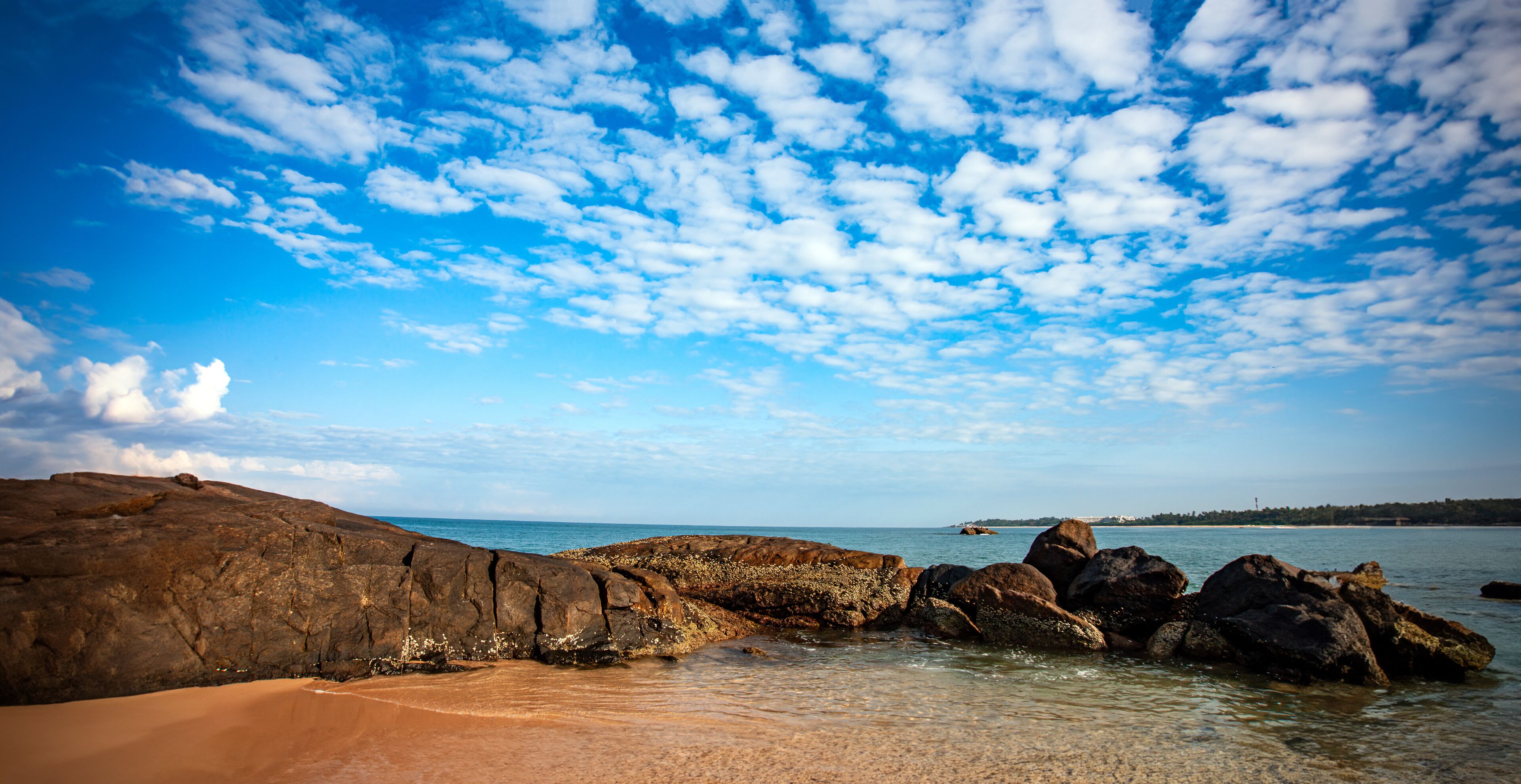 A rocky shoreline with clear blue water and a partly cloudy sky.