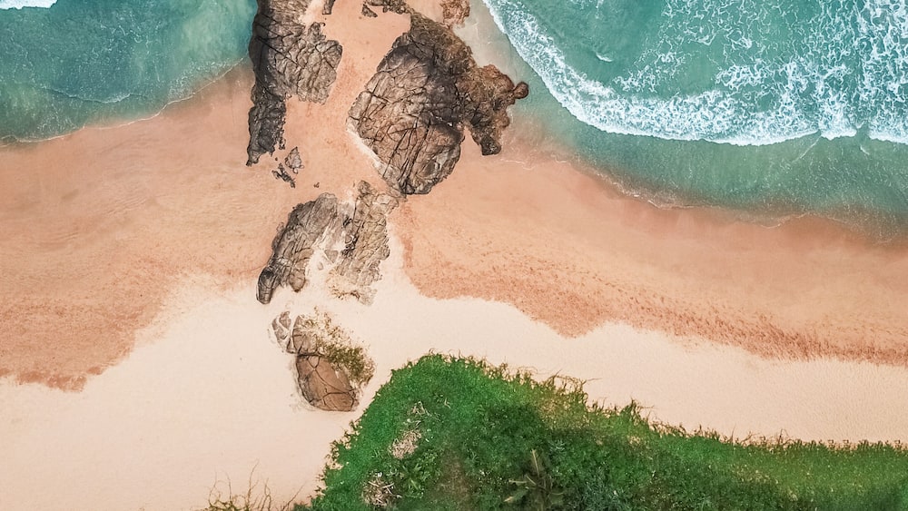 A coastal landscape with a rocky outcrop, sandy beach, and green vegetation.