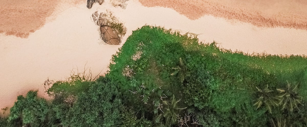 Rannikkomaisema, jossa on kallioinen ulkonema, hiekkaranta ja vihreää kasvillisuutta.