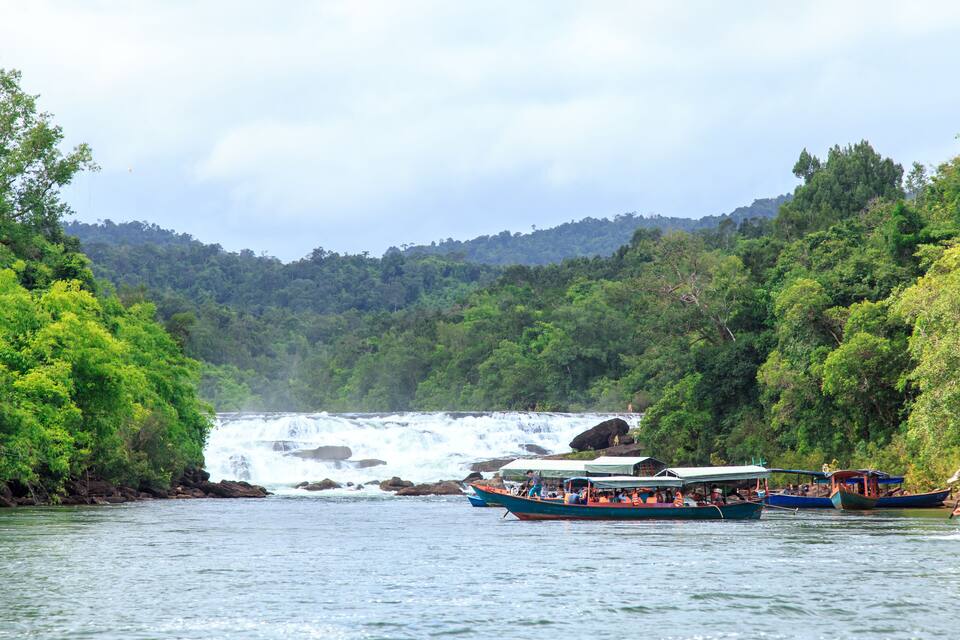 A river with boats and a waterfall in the background.