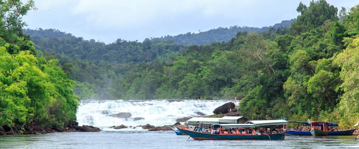 A river with boats and a waterfall in the background.