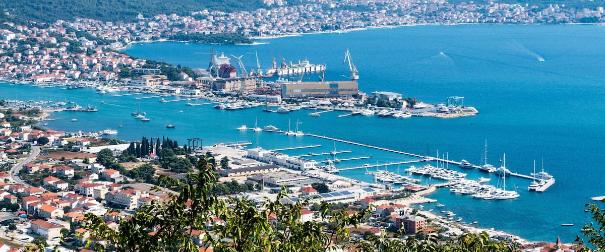 A coastal cityscape with a harbor, boats, and a prominent building with a dome.