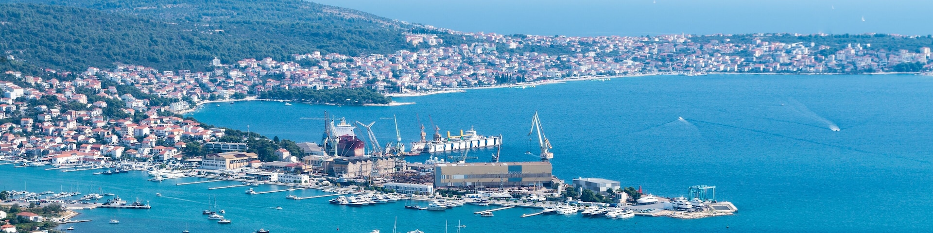 A coastal cityscape with a harbor, boats, and a prominent building with a dome.