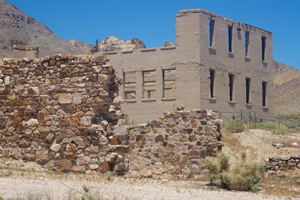 A historical stone building with visible inscriptions, surrounded by a rocky landscape and mountains.