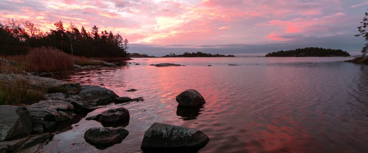 A sunset over a calm lake with rocks and trees.
