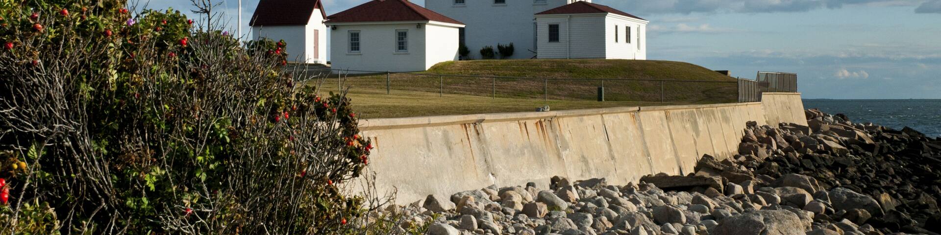 Seagull flies over Watch Hill lighthouse at low tide in early evening in summer, in Rhode Island.