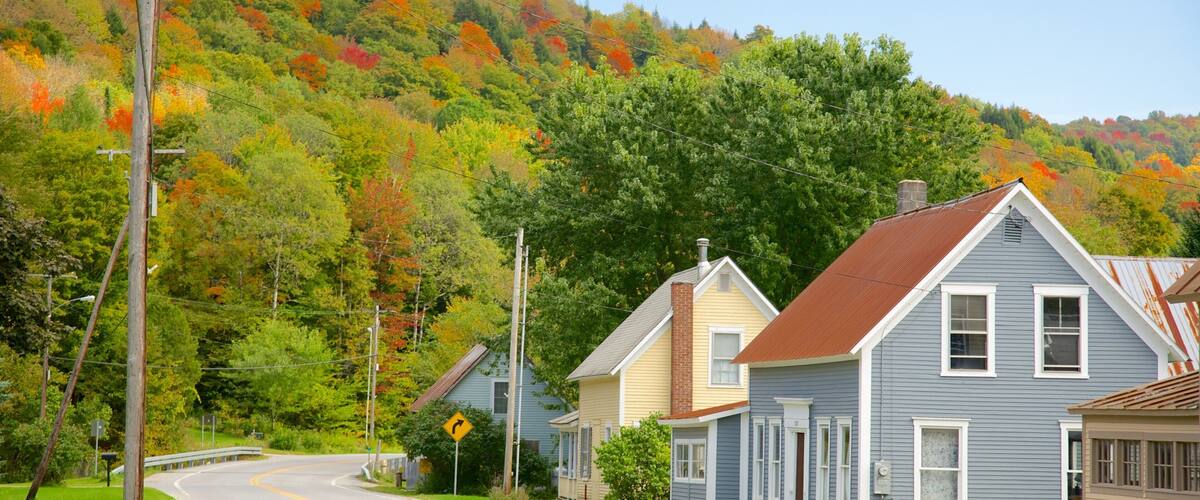 A rural road curving through a village with houses and autumn-colored trees.