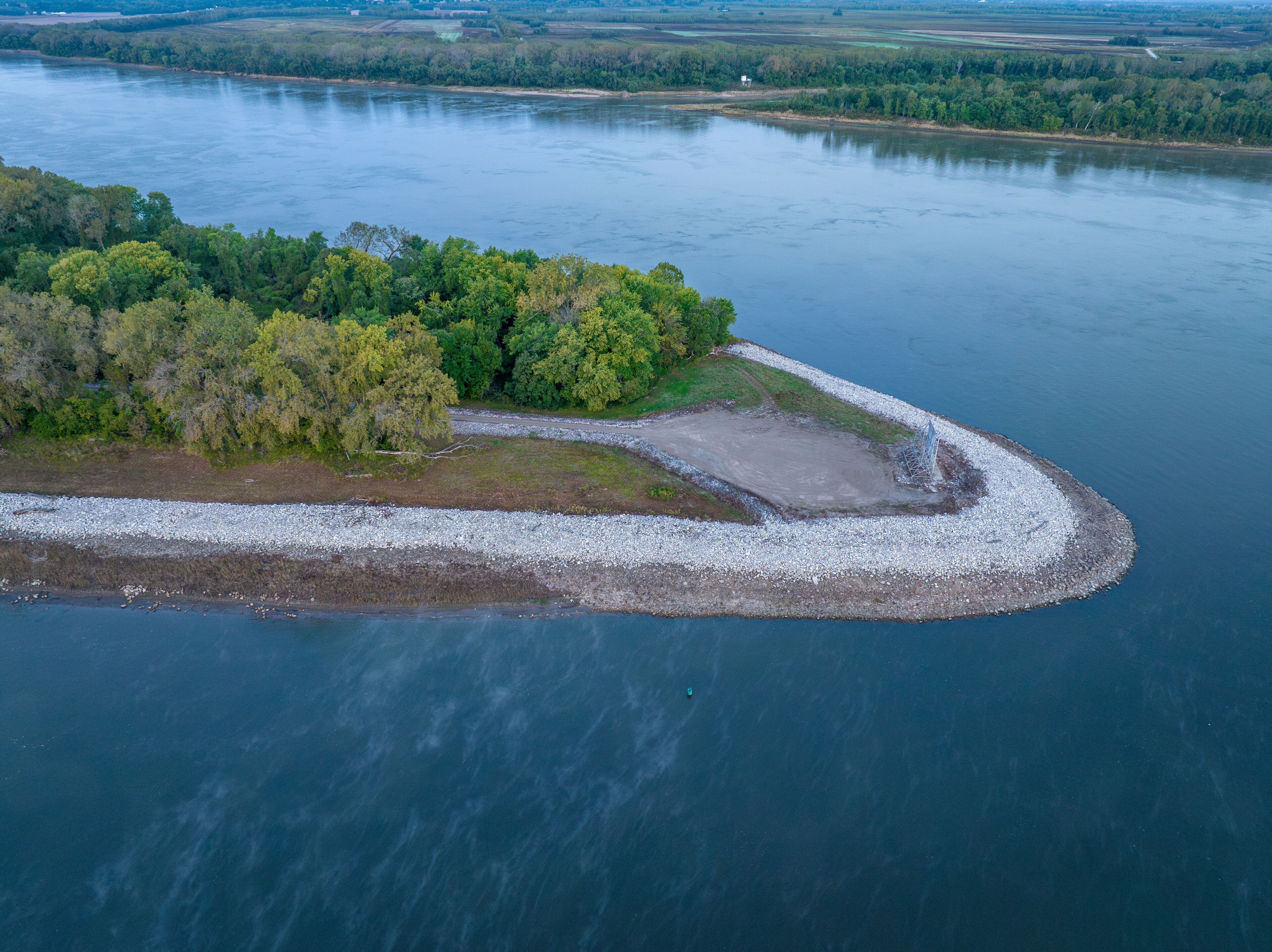 An aerial view of a river with a small island covered in trees and a rocky shoreline.