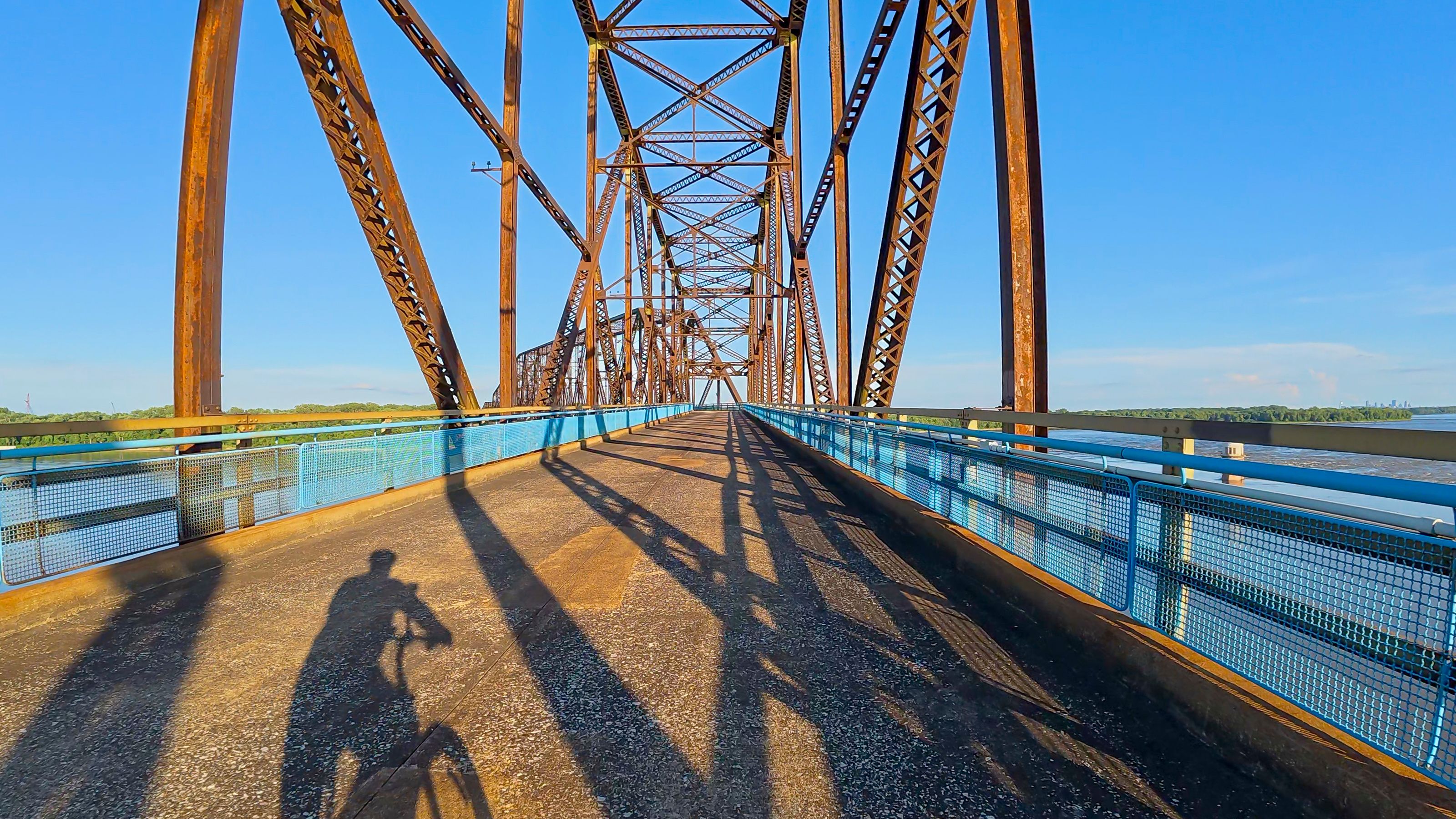 Un puente de acero con barandillas azules y sombras de personas en la pasarela.