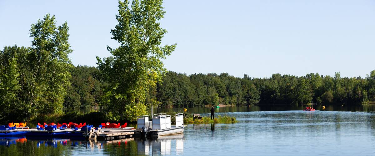 A calm lake with boats docked on the left, surrounded by dense forest.