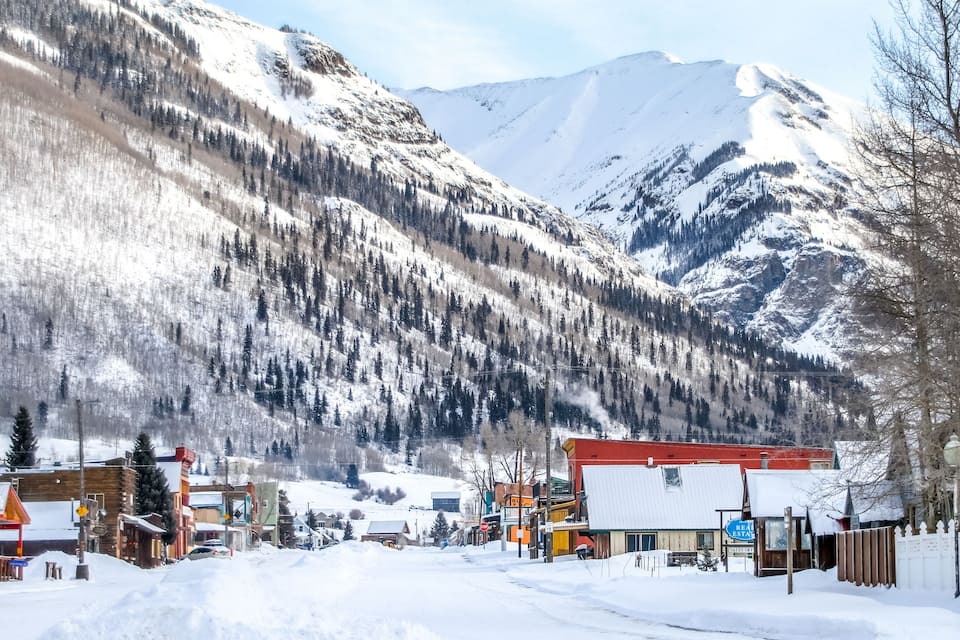 Une ville enneigée, avec des bâtiments, une montagne en arrière-plan et un ciel dégagé.