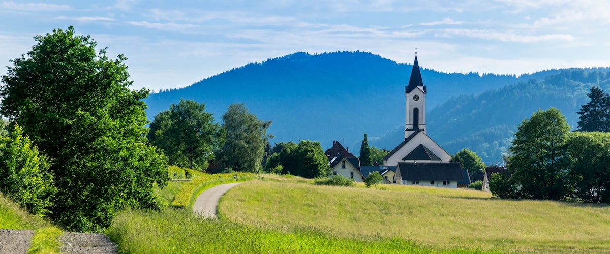 A church with a tall steeple, surrounded by lush green fields and a mountain in the background.