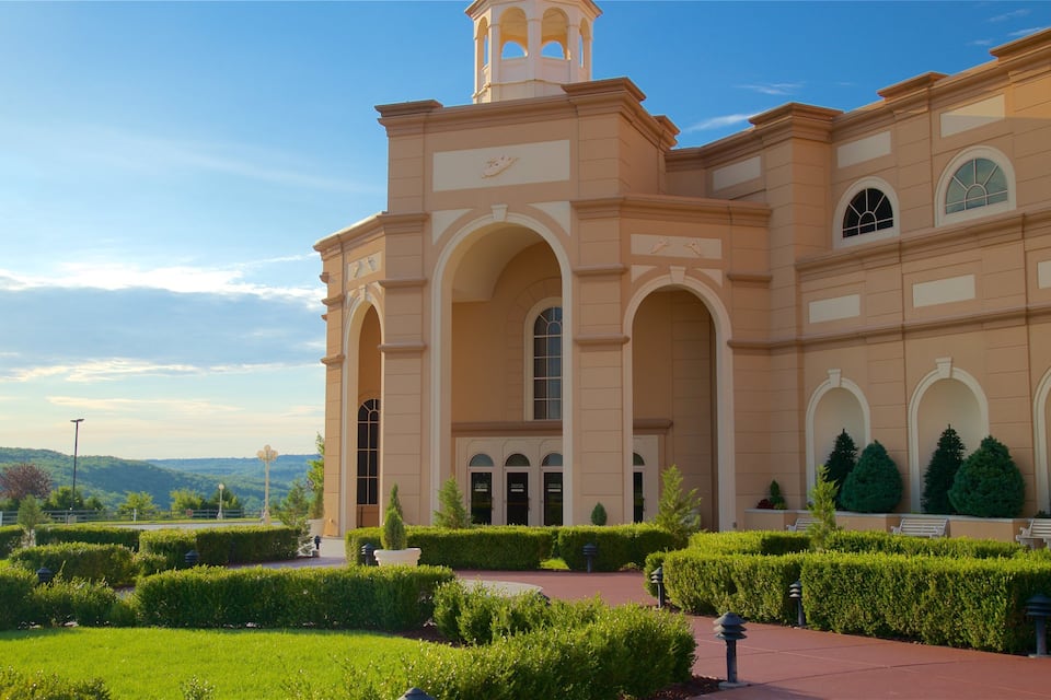 A large, beige building with arched windows and a bell tower, surrounded by well-manicured hedges and a clear sky.