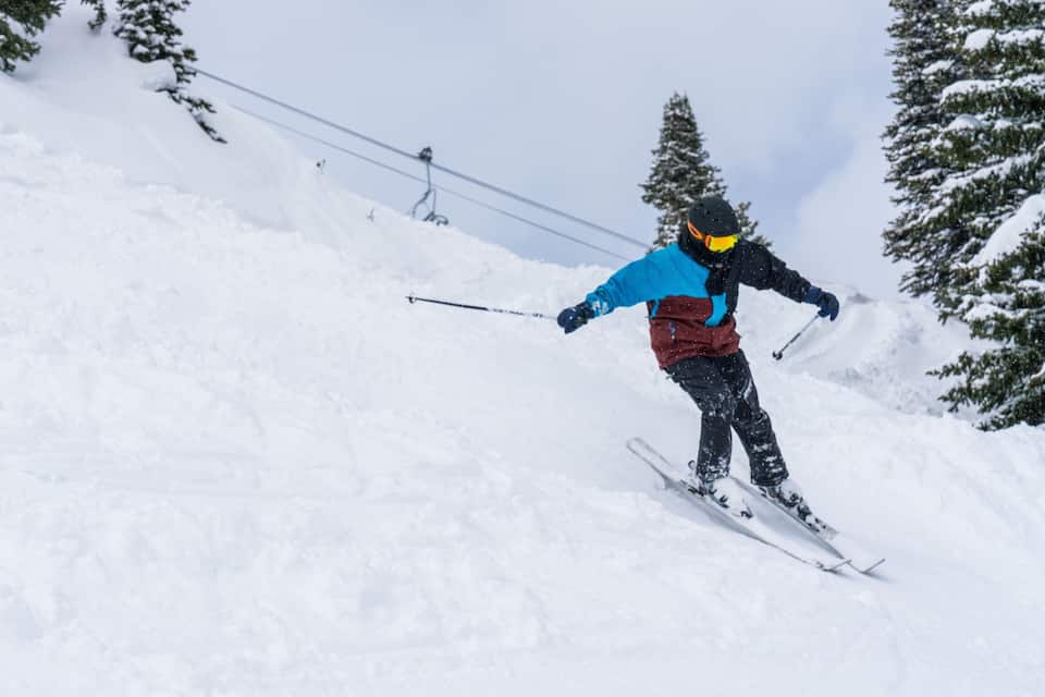 A skier on a snowy slope with trees and ski lifts in the background.