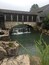 A stone bridge over a pond with a waterfall, surrounded by rustic wooden buildings and greenery.
