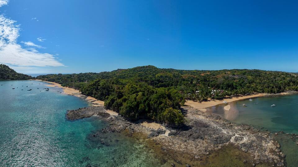 A coastal landscape with a sandy beach, clear turquoise waters, and a small island with dense greenery.