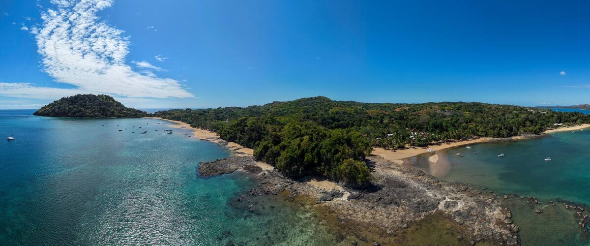 A coastal landscape with a sandy beach, clear turquoise waters, and a small island with dense greenery.