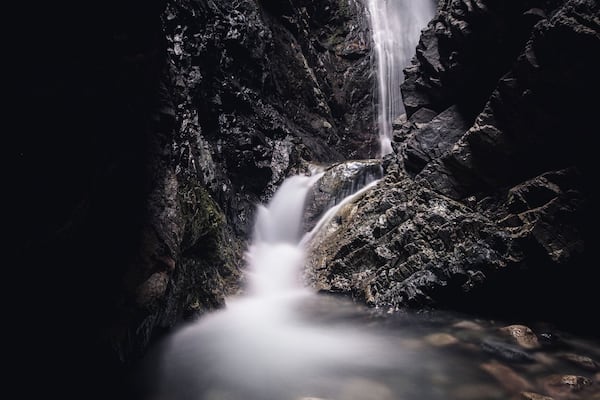 A waterfall cascading down a rocky cliff into a pool of water surrounded by large boulders.