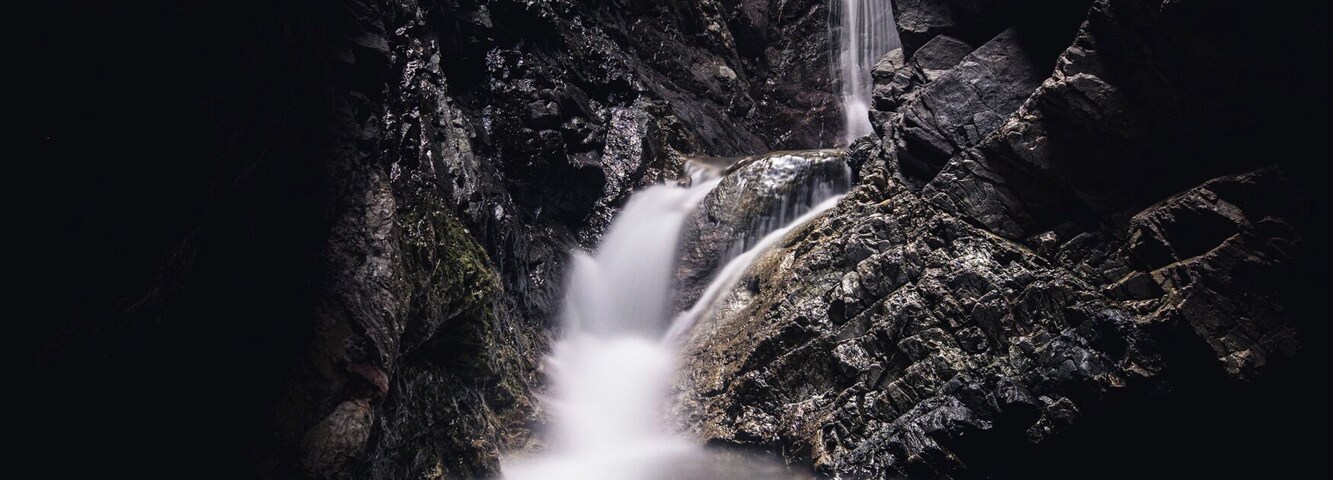 Uma cascata despencando de um penhasco rochoso em direção a um lago, cercado por grandes pedras.