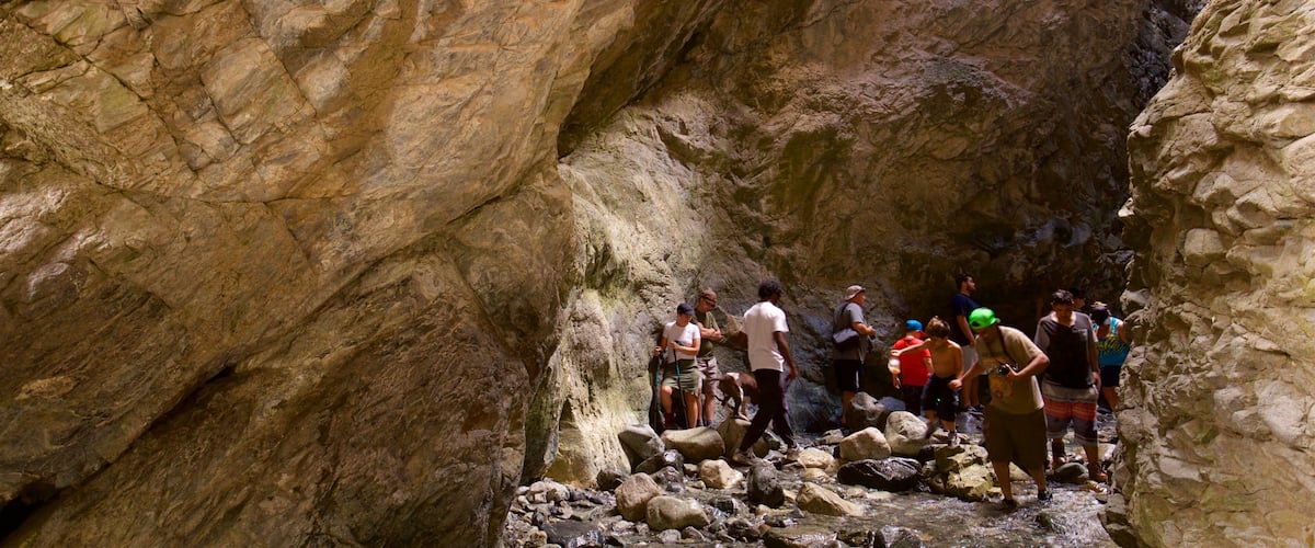 A group of people hiking through a rocky canyon with steep walls and a stream at the bottom.