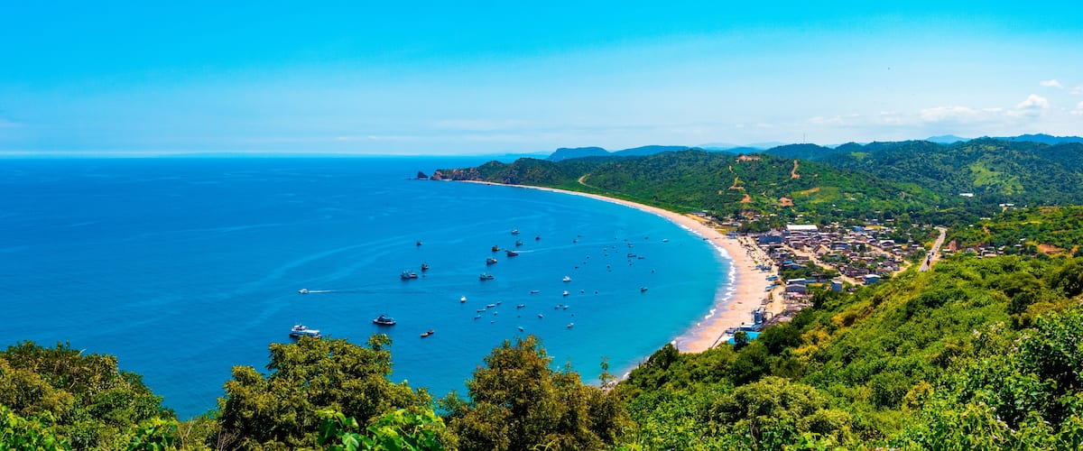 A coastal town with a beach, boats, and lush green hills.