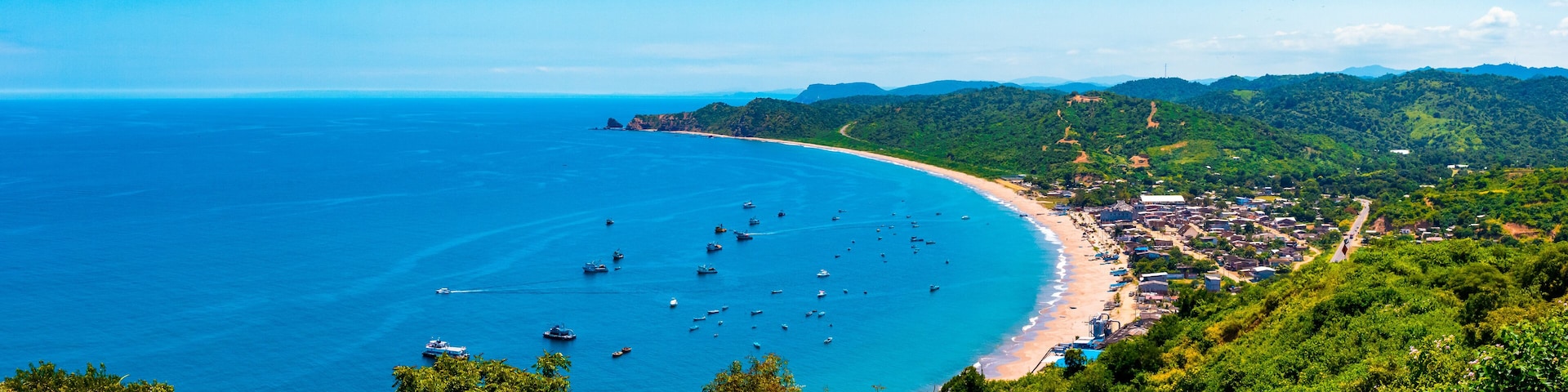 A coastal town with a beach, boats, and lush green hills.