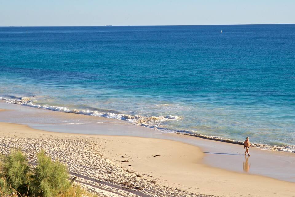 Een strand met helderblauw water, een zandstrand en een persoon die langs de waterlijn loopt.