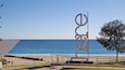 A beach with a large metal sculpture, a clear blue sky, and the ocean in the background.