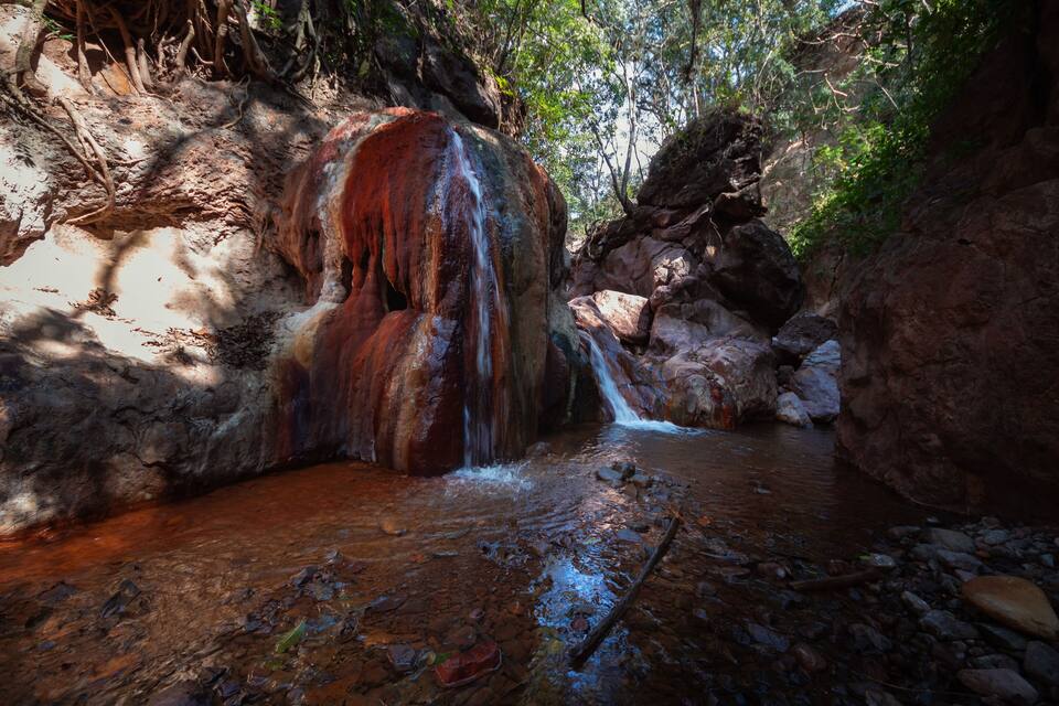 A waterfall in a forested area with rocky terrain and a stream.