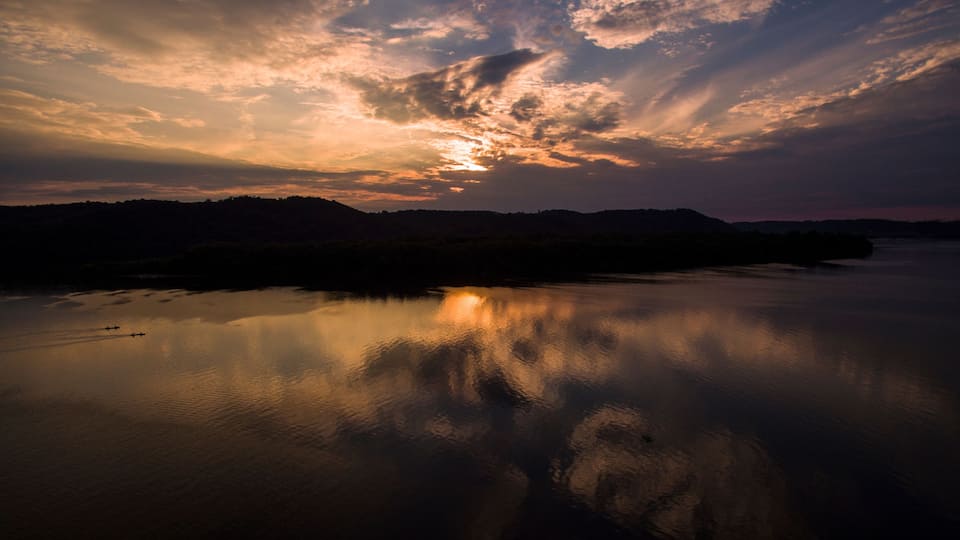 A sunset over a calm river with reflections of clouds, surrounded by hills.