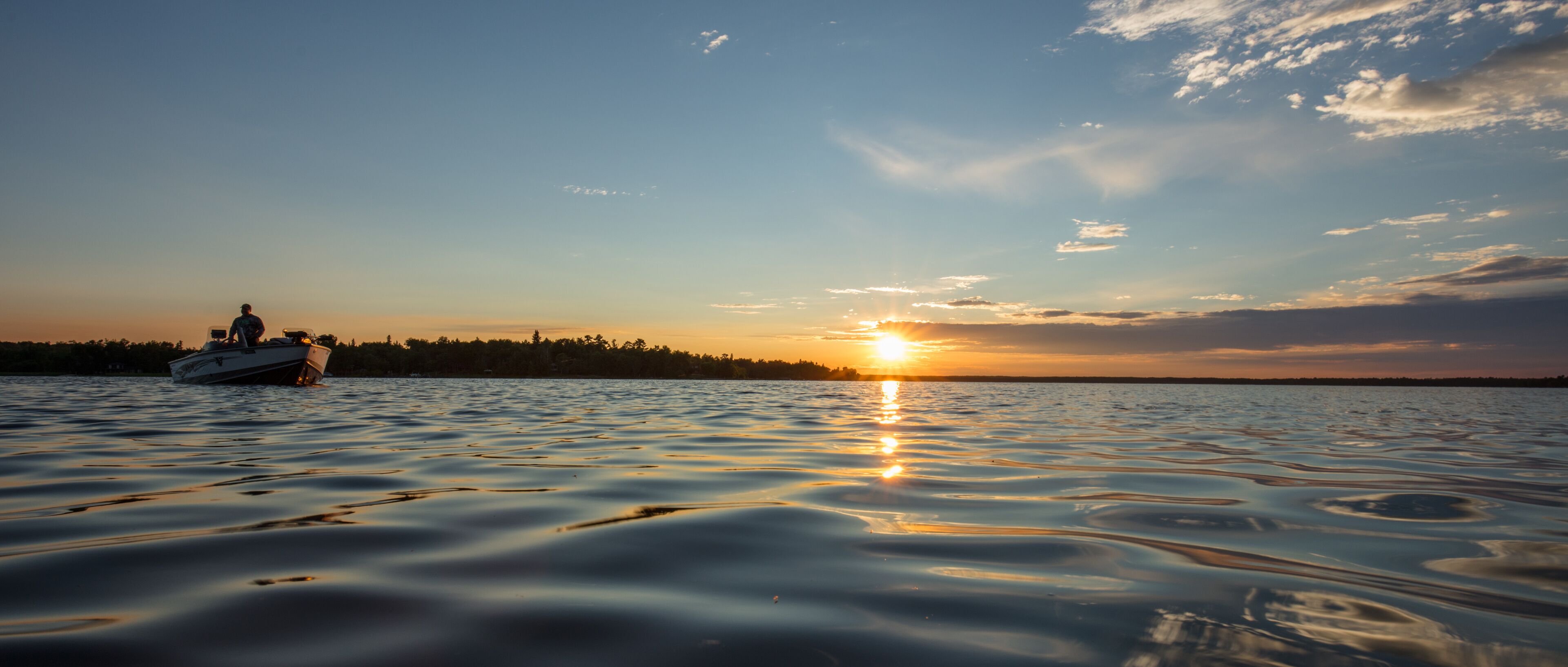 A boat on calm water with a sunset in the background.