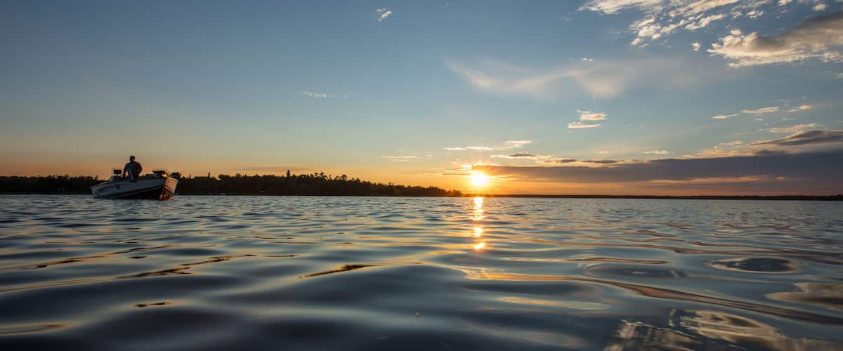 A boat on calm water with a sunset in the background.