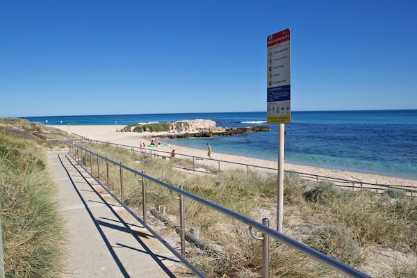 A coastal walkway with a sign indicating general warnings and life-saving services.