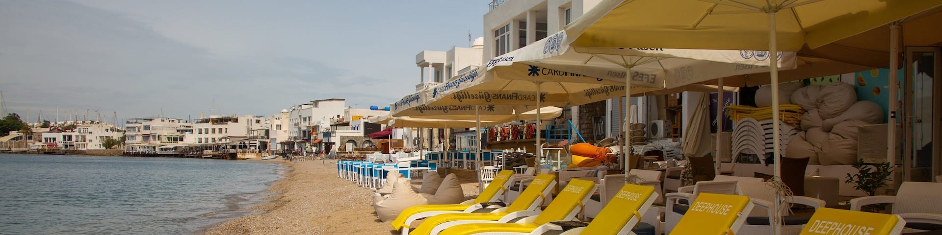 A beach with yellow lounge chairs and umbrellas, a pebble beach, and buildings in the background.