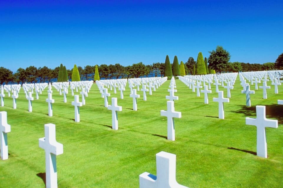 A cemetery with rows of white crosses on green grass under a clear blue sky.
