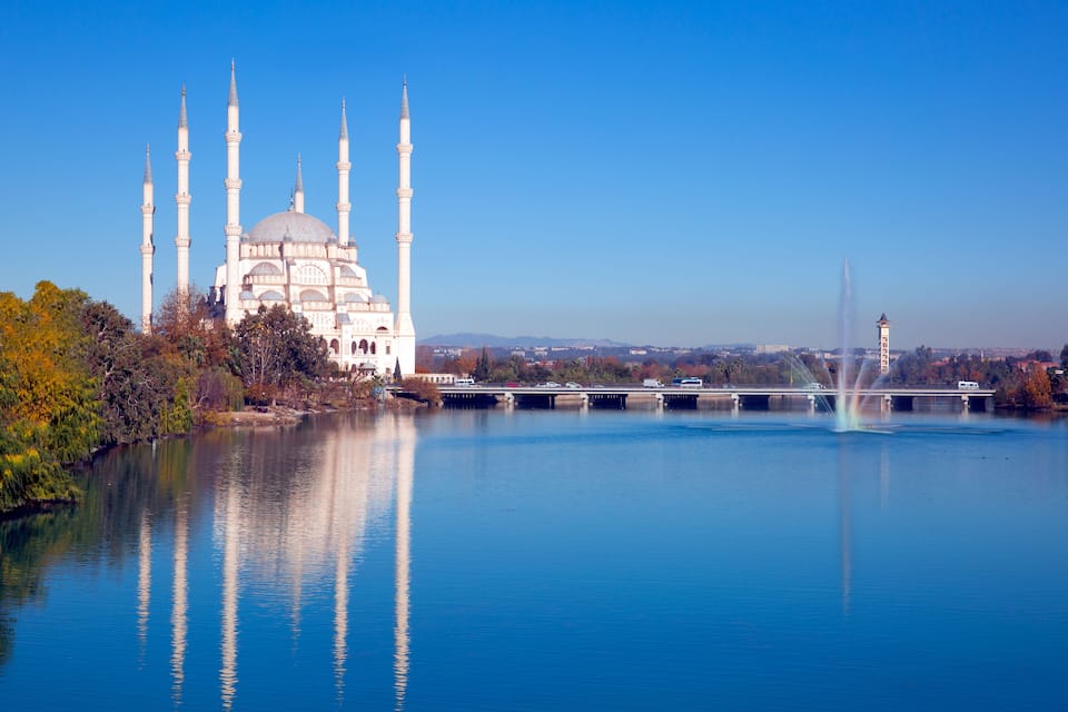 A mosque with multiple minarets, a large dome, and a reflection in the water.