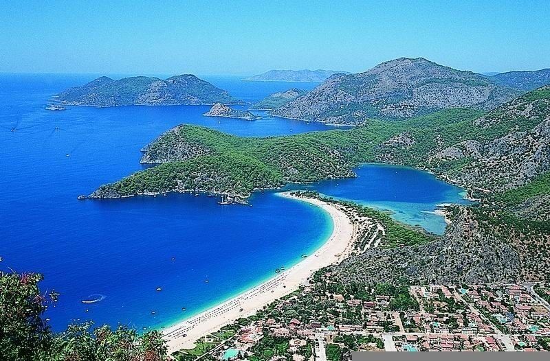 A coastal landscape with a curved bay, a sandy beach, and a densely populated area with buildings.