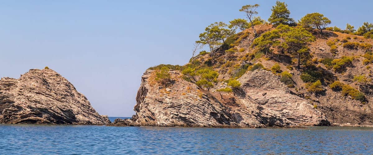 A rocky coastline with clear blue water and sparse vegetation.