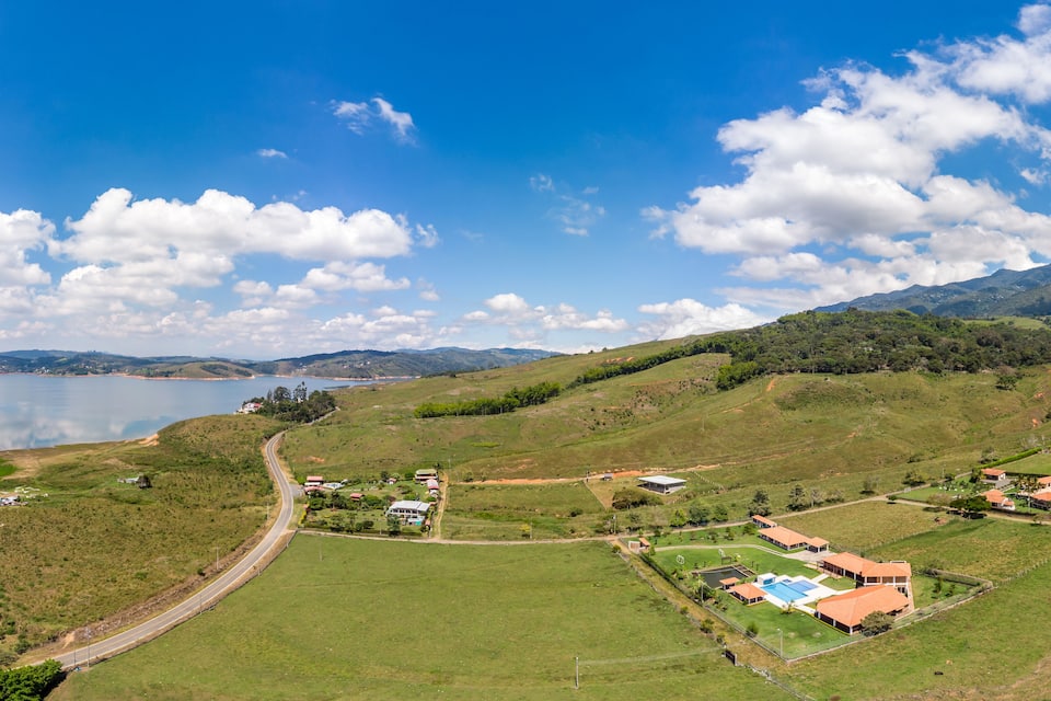 A coastal landscape with a winding road, green fields, a swimming pool, and distant mountains.