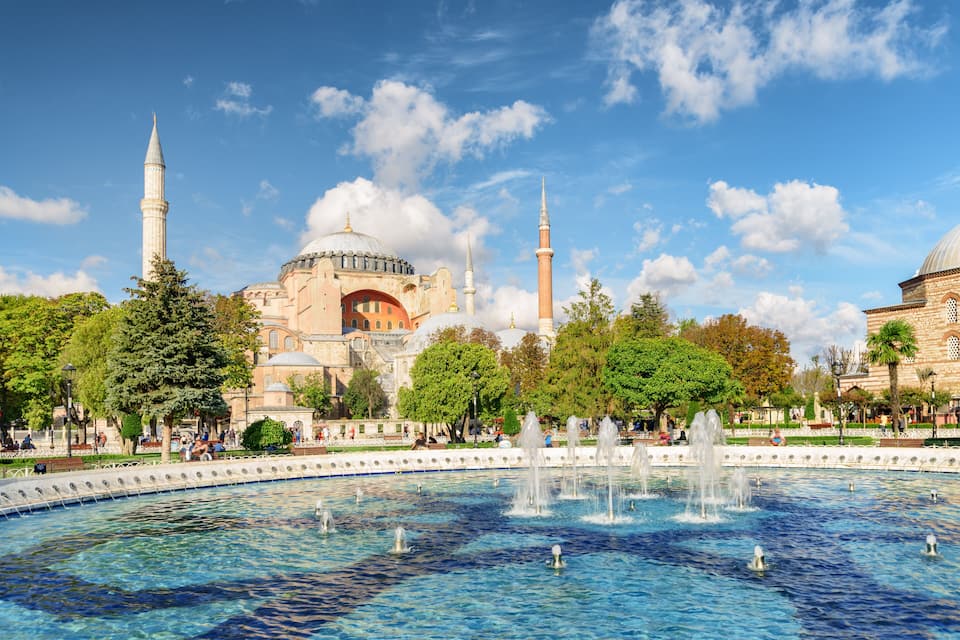 Un bâtiment historique doté de coupoles et de minarets, entouré d’arbres et agrémenté d’une fontaine.