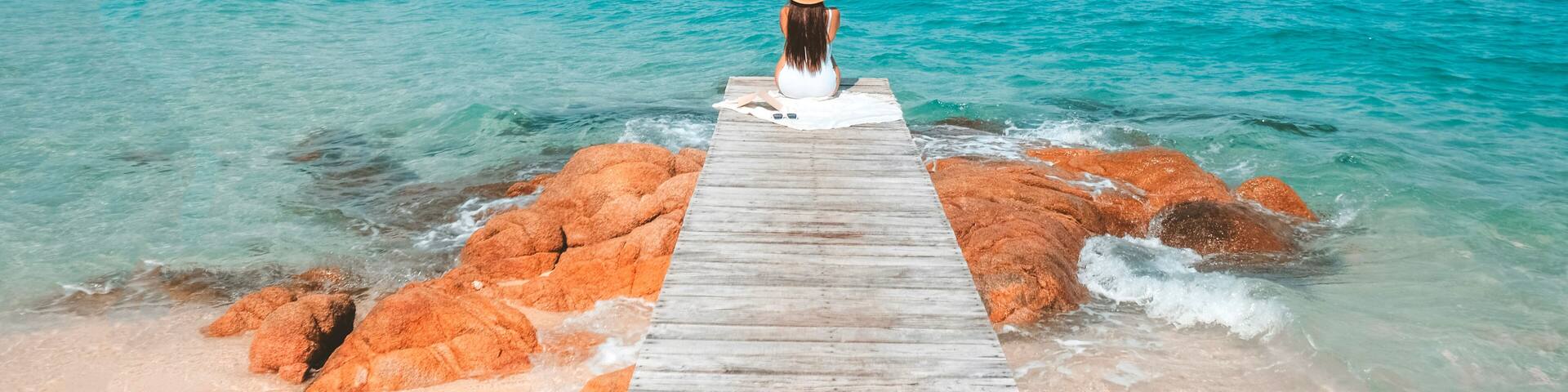 Alone woman sitting by the sea enjoying the blue ocean view at the beach. Travel pictures and vacation at Kho Mun Nork, Thailand.